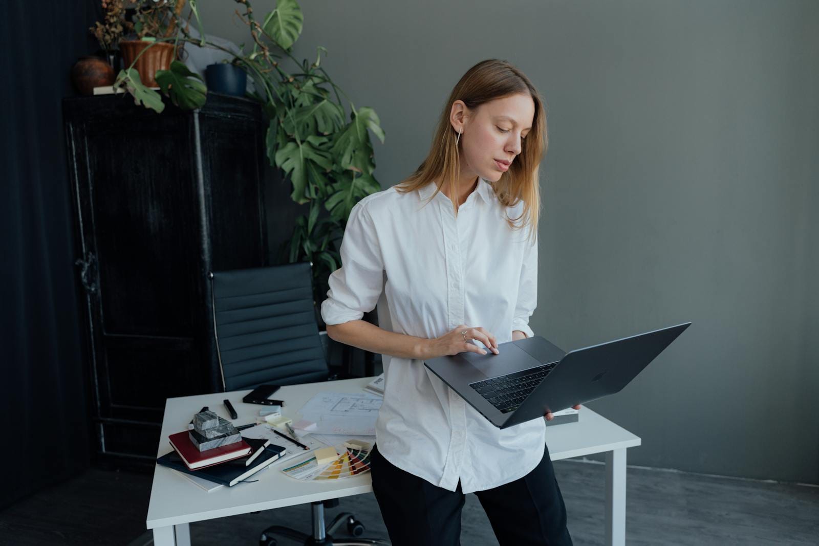 Young woman in white shirt working from home on laptop with plants