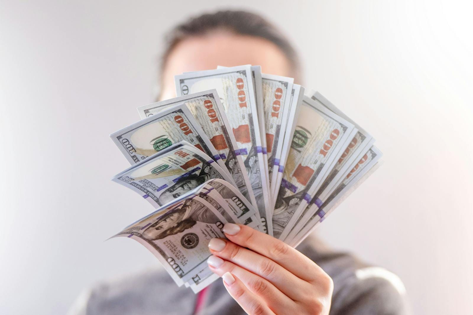 Hand holding fan of US dollar bills, illustrating financial success