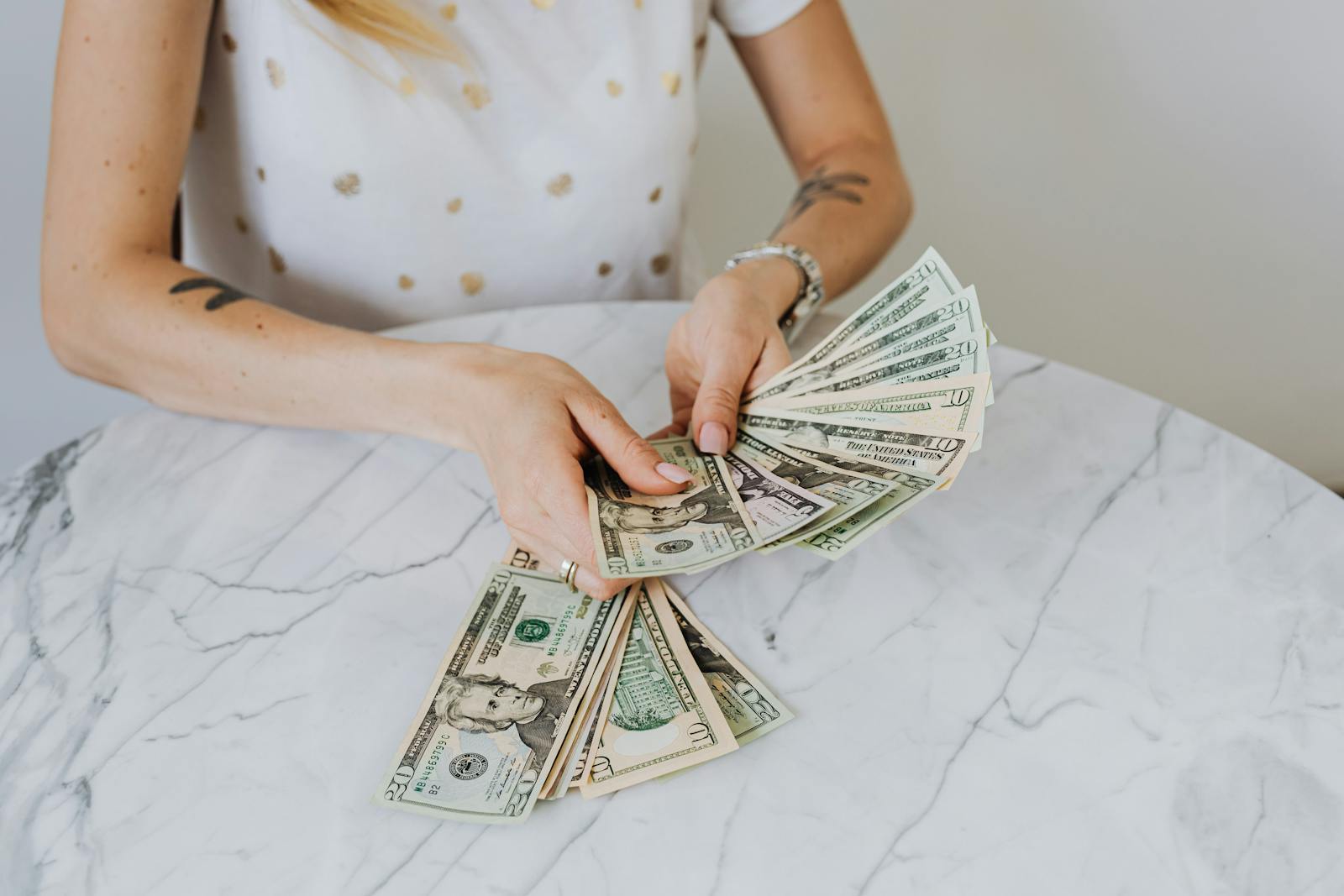 Person counting US dollar bills on marble table, illustrating wealth concept