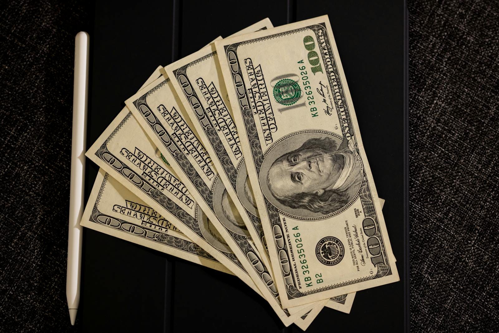 Spread of US dollar bills with stylus, illustrating finance and technology