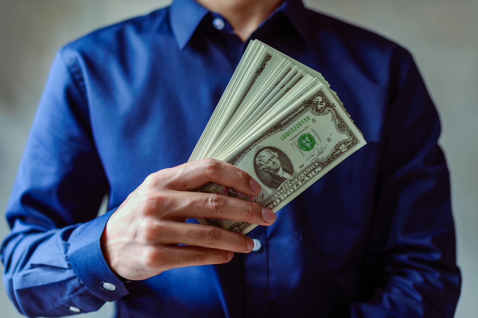 Person in blue shirt holding multiple dollar bills, illustrating earnings