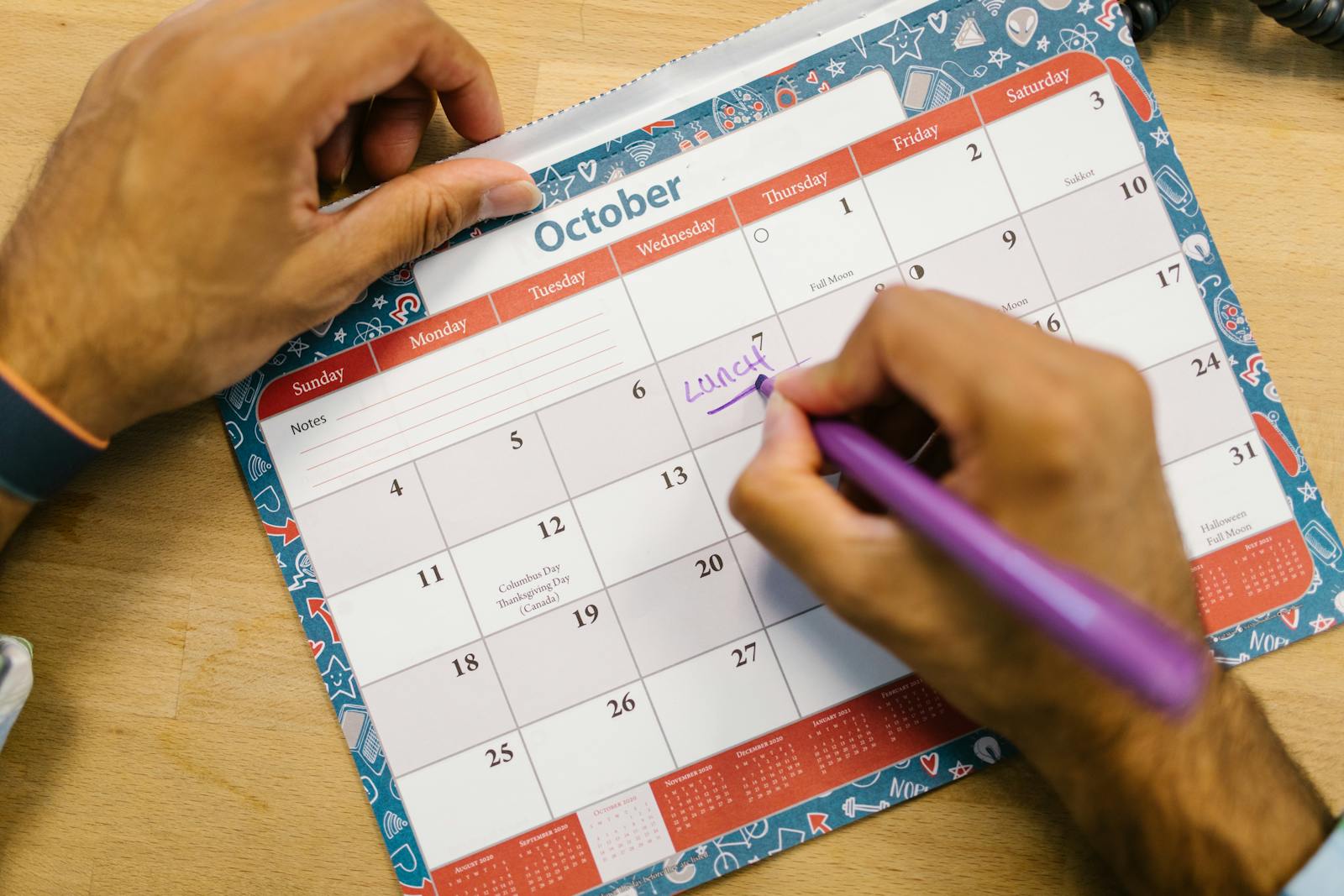 Person writing reminder on calendar with pen, illustrating content planning