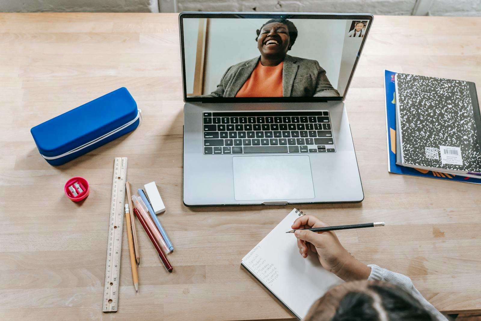Top view of person taking notes during online lecture, illustrating focused learning