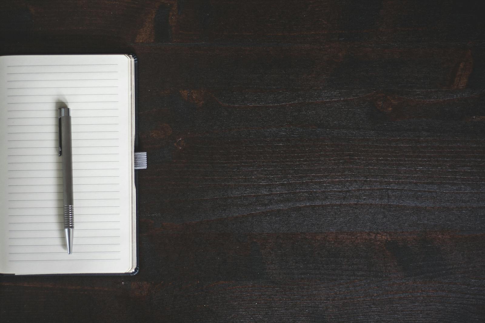 Minimalist open notebook with pen on dark wooden desk