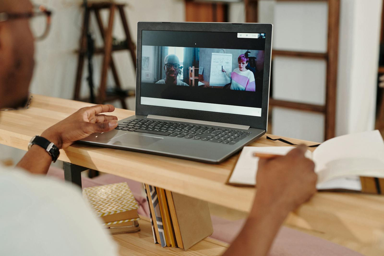 Adult on laptop video conferencing, taking notes during remote meeting