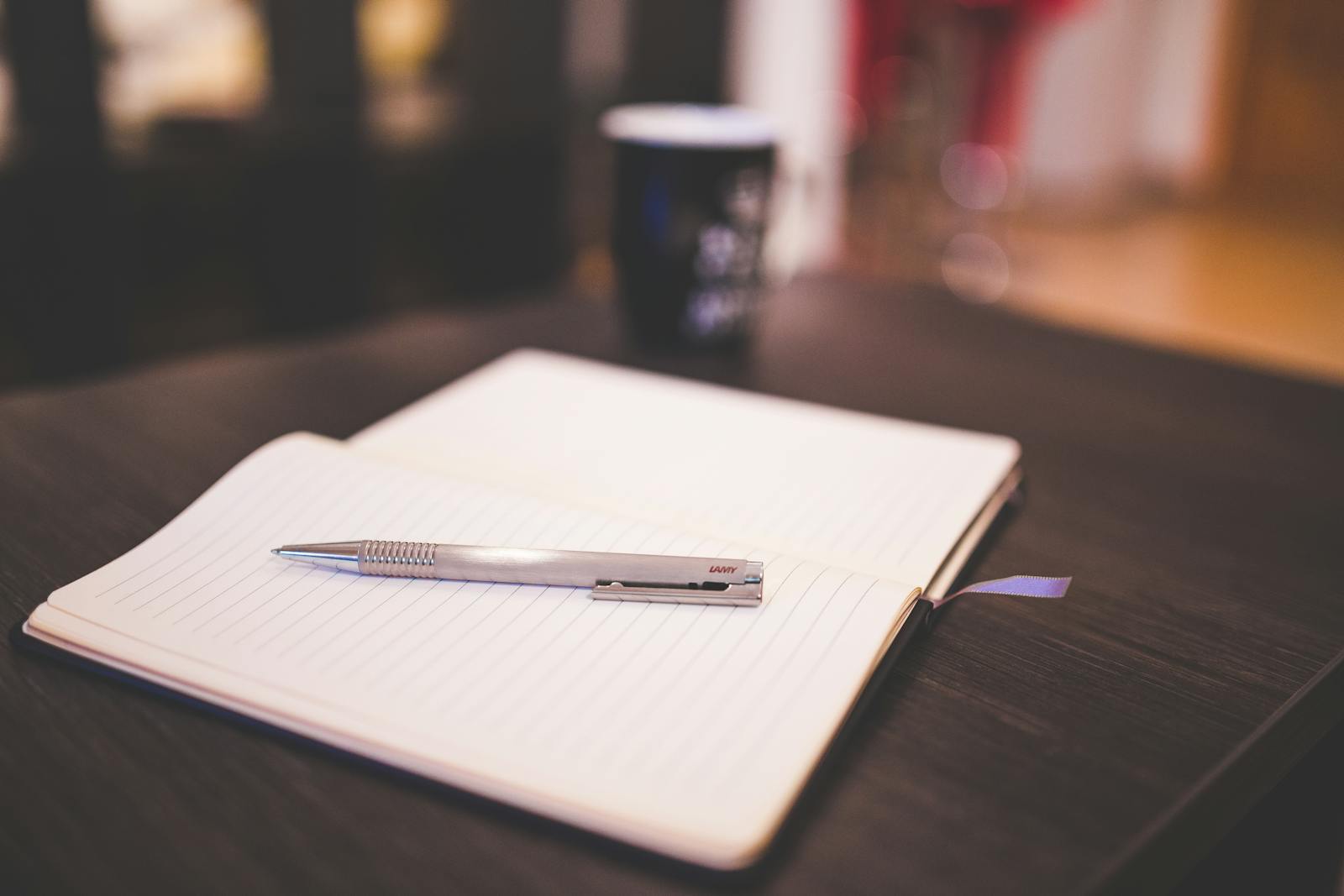 Open lined notebook with silver pen on dark wooden table