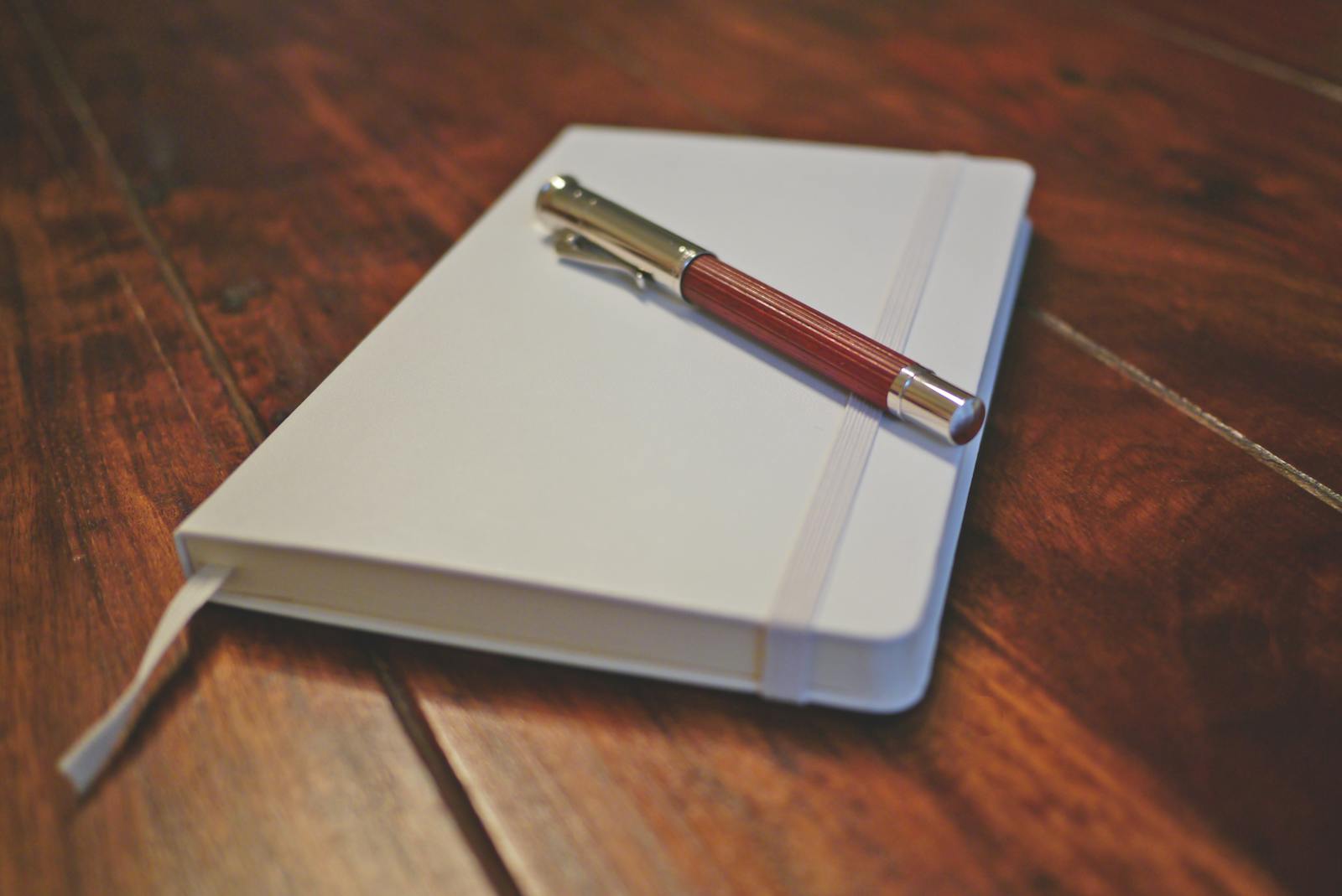 Notebook and pen on wooden desk, minimalist stationery arrangement
