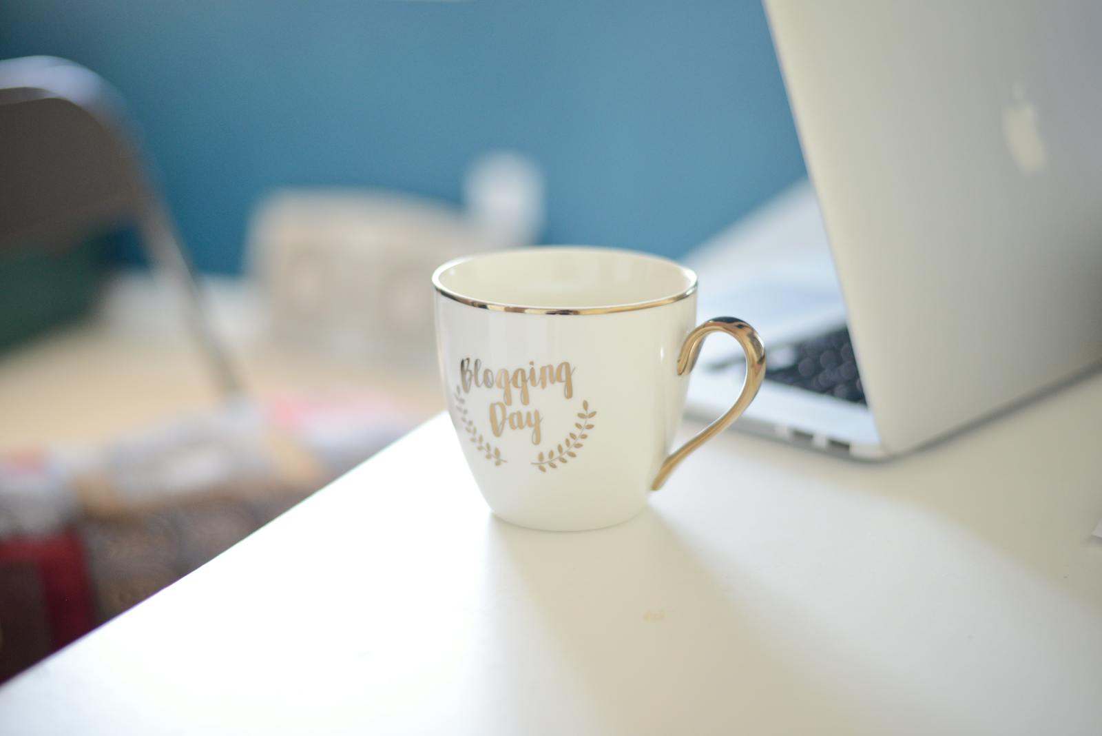 Coffee cup labeled blogging day on white desk beside laptop, illustrating creator workflow