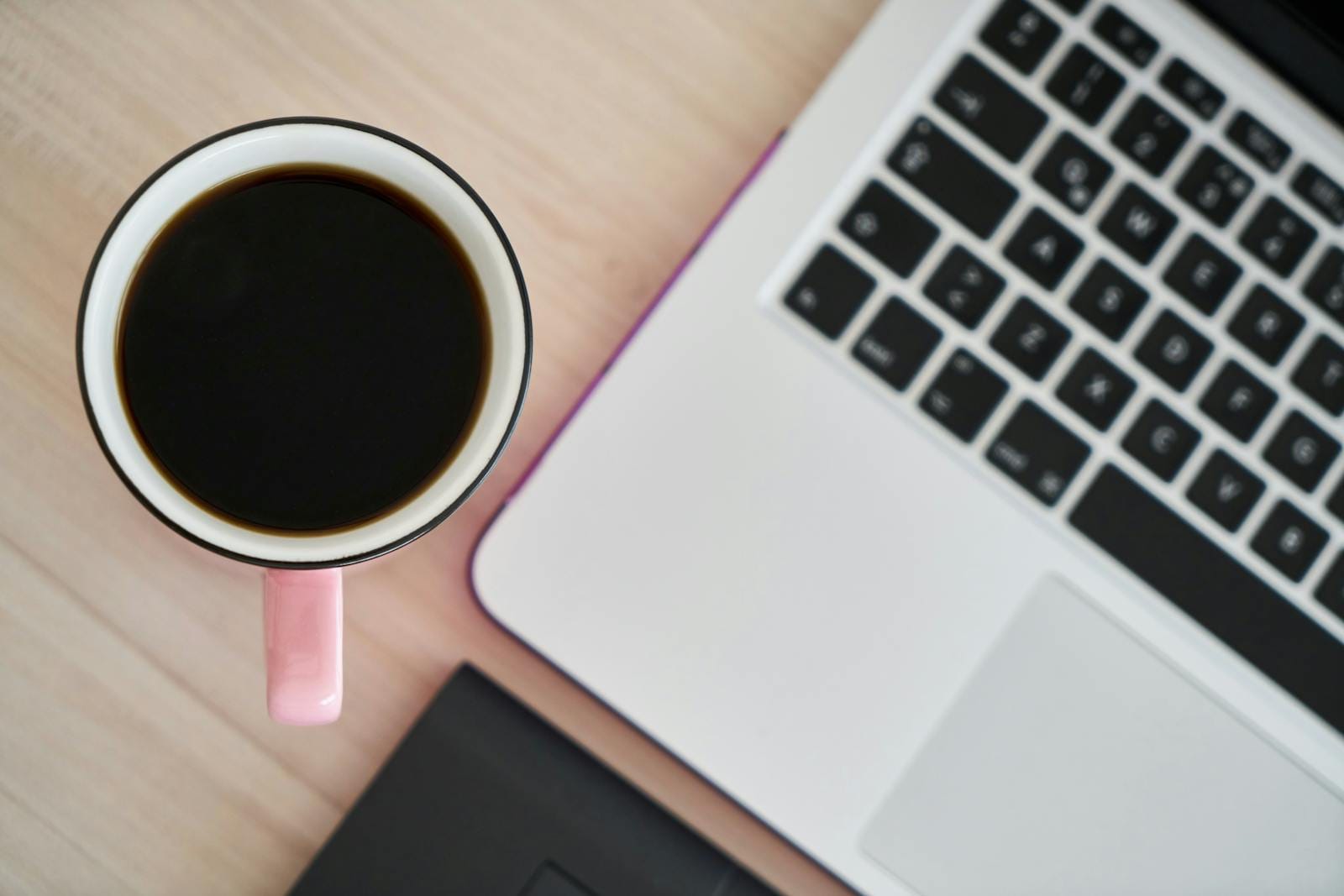Overhead view of pink coffee mug and laptop on wooden desk, illustrating productivity
