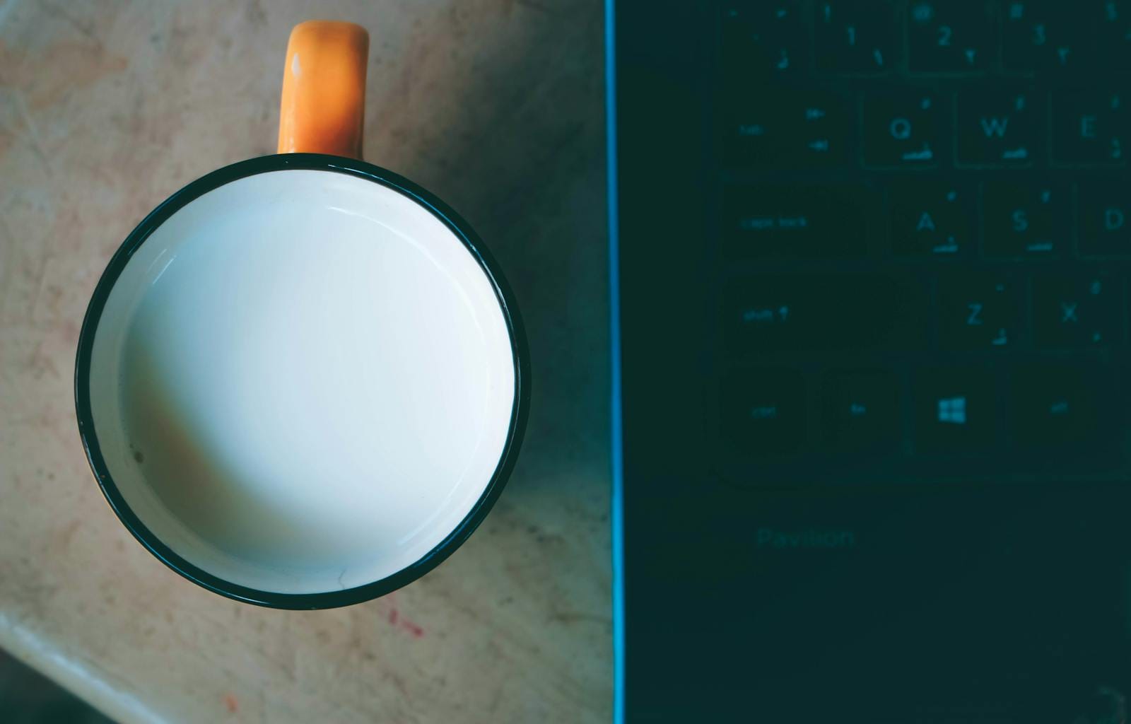 Top-down view of coffee mug beside laptop keyboard, illustrating creator setup