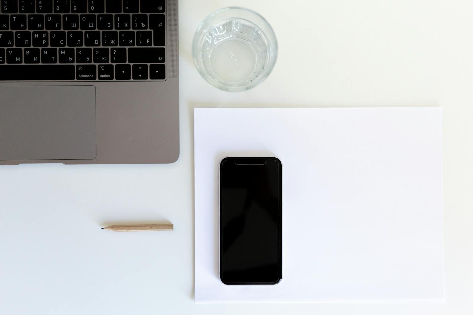 Smartphone on white paper with laptop and water glass at modern workplace