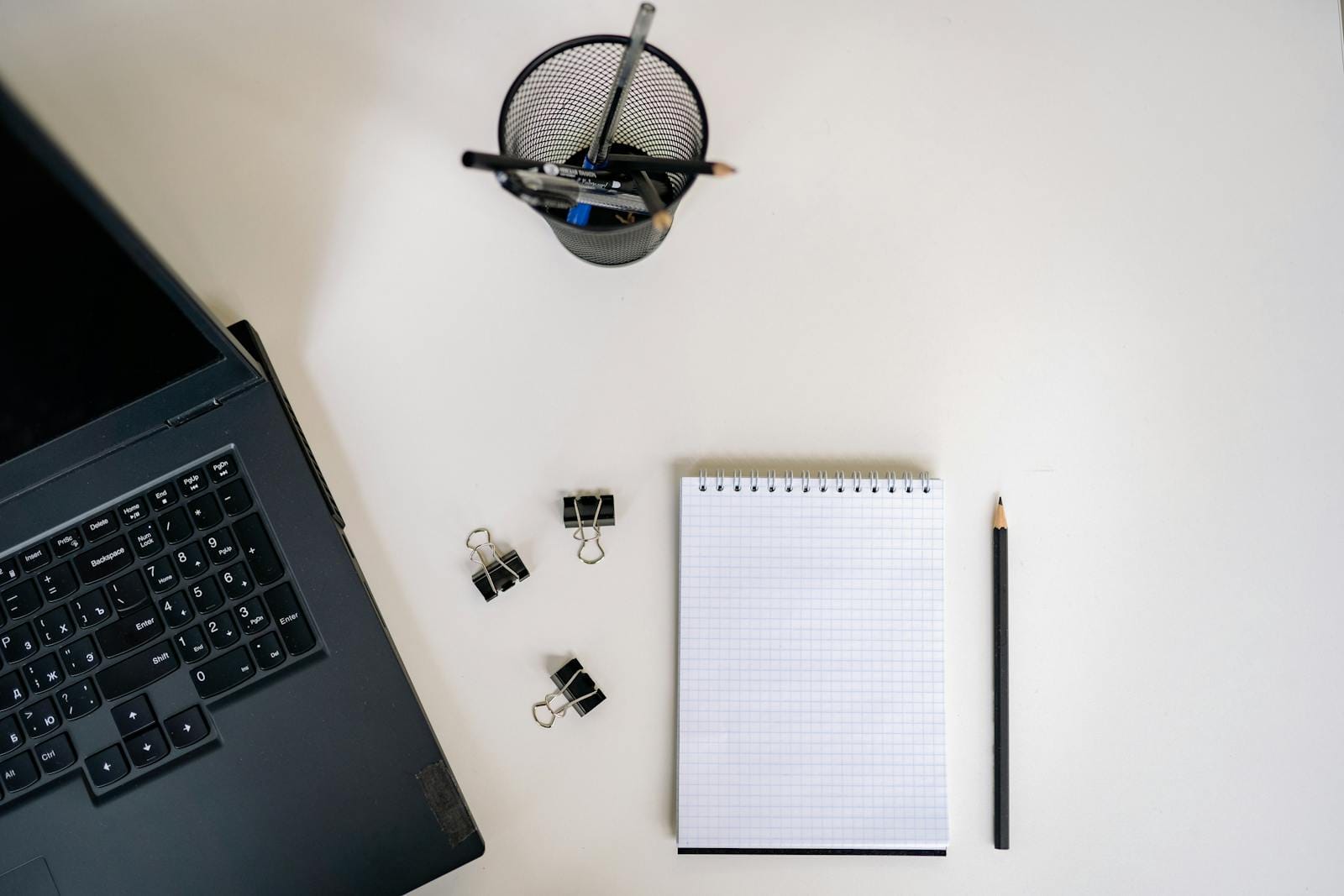 Top view of office setup with laptop, notepad, pencils on white desk