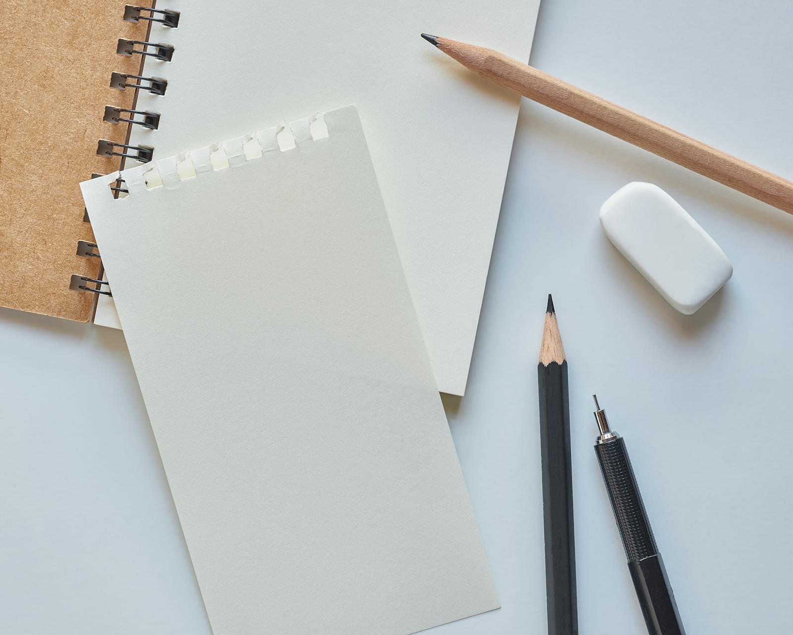 Flat lay of spiral notebook, pencils, pen, and eraser on white background