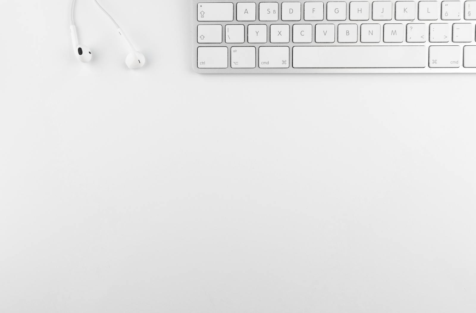 Top view white minimalist desk featuring keyboard and earphones
