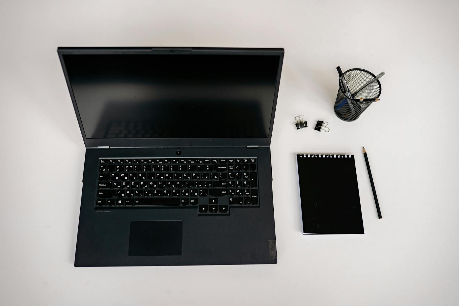 Flat lay of laptop, notepad, pencil, and office supplies on white desk