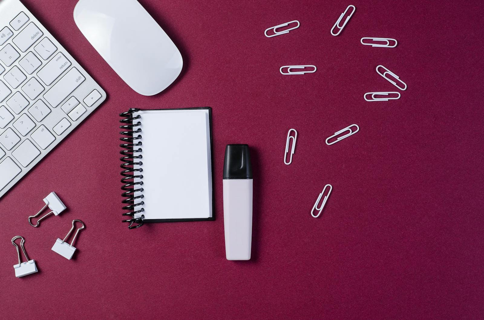 Office stationery on burgundy desk with keyboard, notebook, paper clips