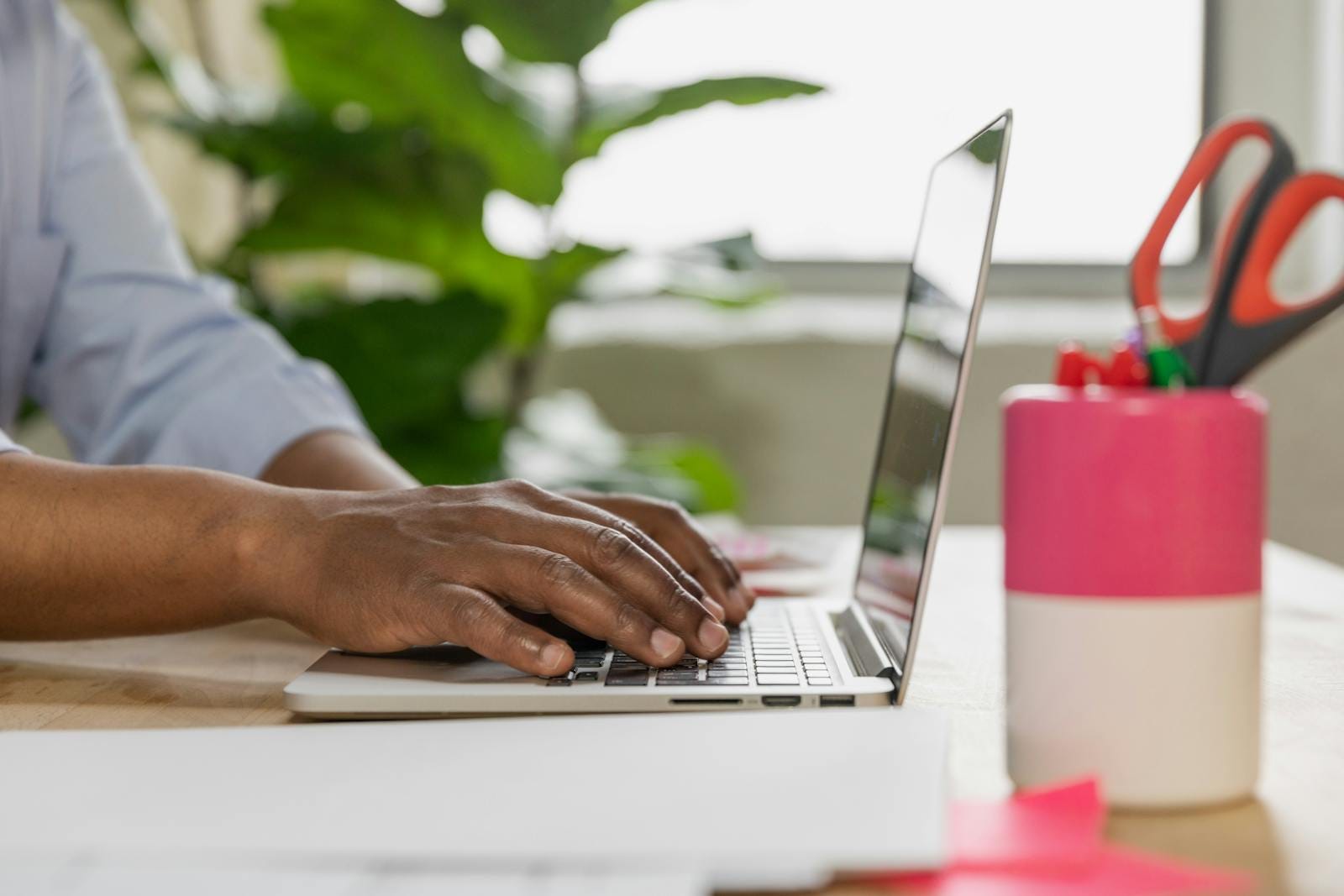 Close-up of male hands typing on laptop with office supplies and plants