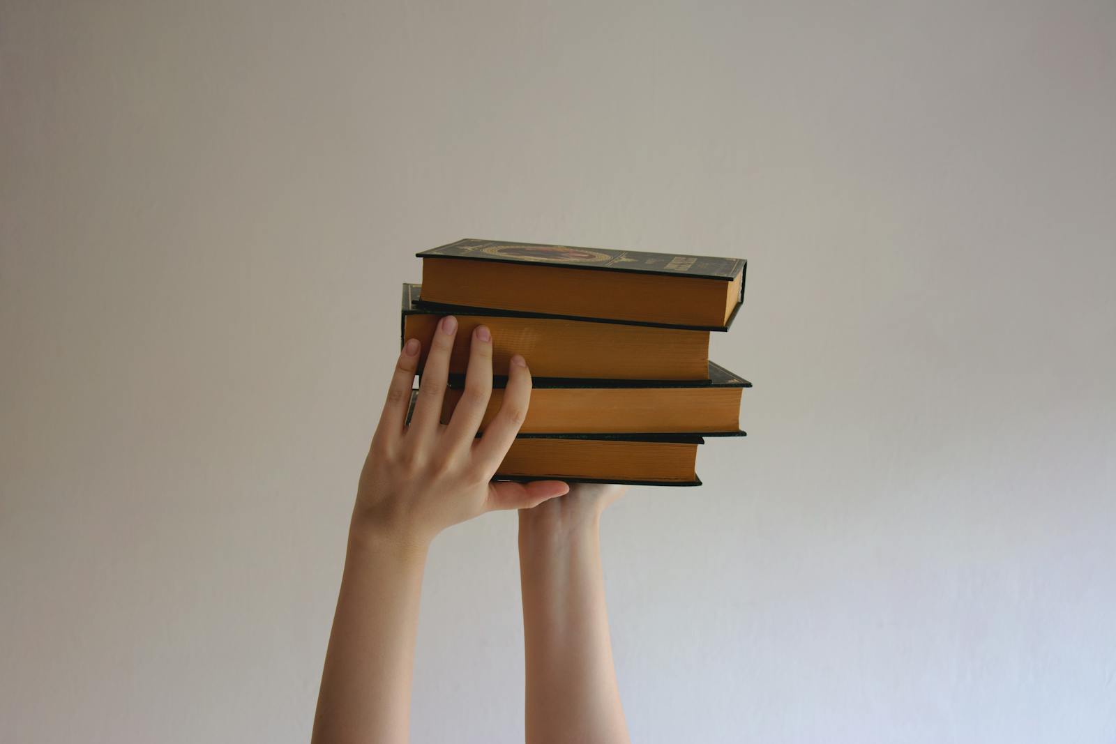 Hands holding stack of hardbound books, illustrating learning