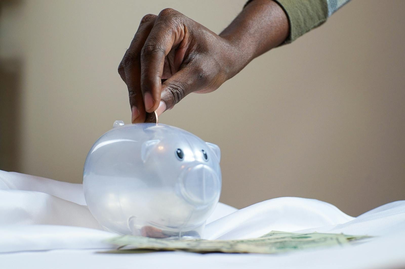 Hand placing coins into transparent piggy bank, illustrating saving money