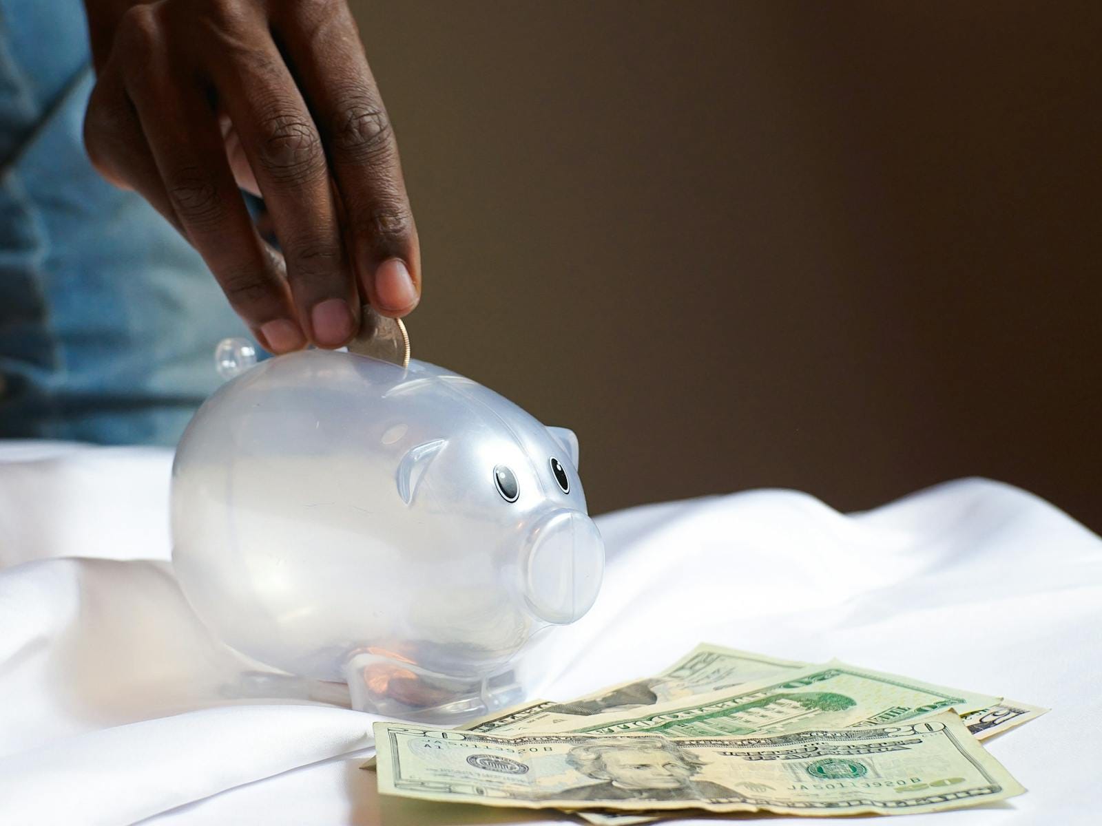 Hand placing coin in piggy bank with dollar bills, illustrating savings finance