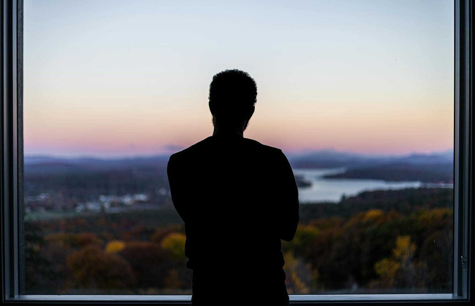 Silhouetted figure by window viewing sunset landscape, illustrating reflection