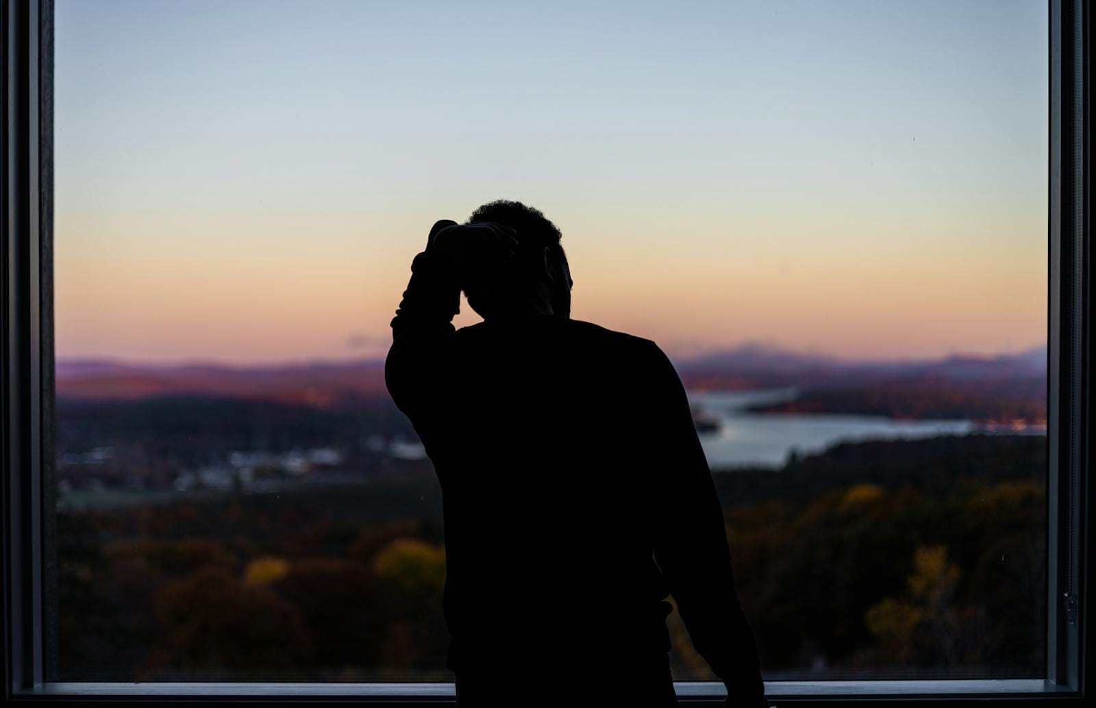 Silhouette at window gazing at lake and mountain sunset, illustrating goals