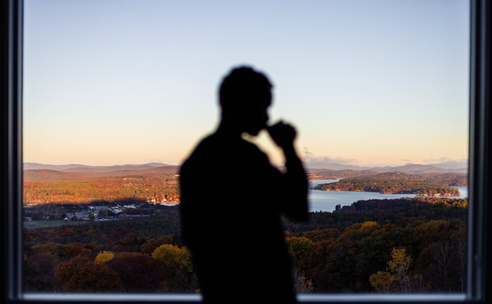 Silhouette drinking by window with scenic sunset, illustrating evening reflection