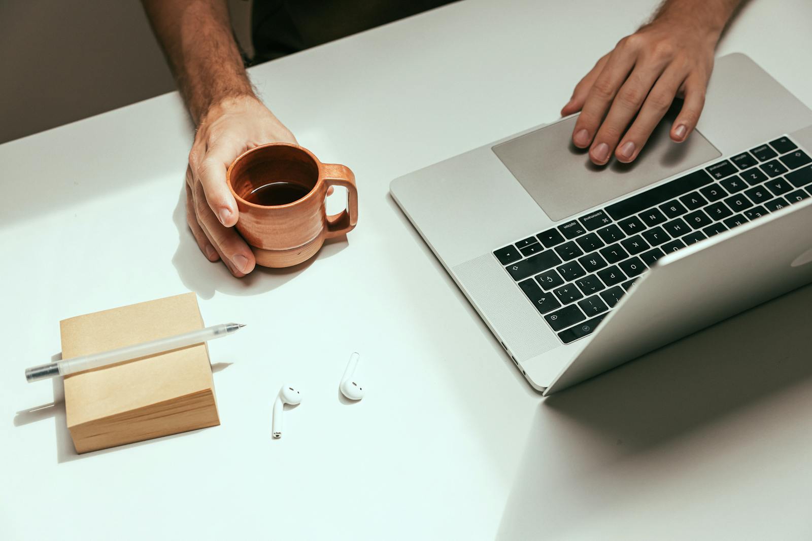 Minimalist workspace with laptop, coffee mug and AirPods, illustrating systems-built late-stage creator work