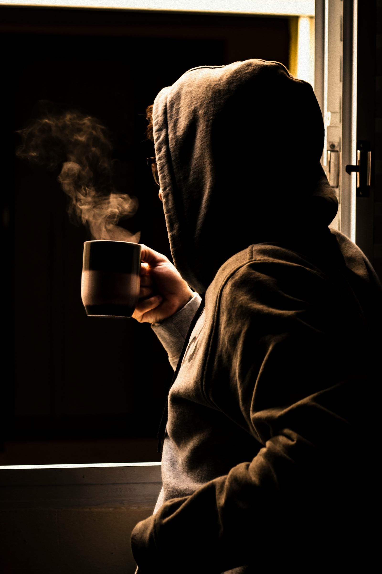 Person in hoodie with coffee at window contemplating, illustrating mindset shift
