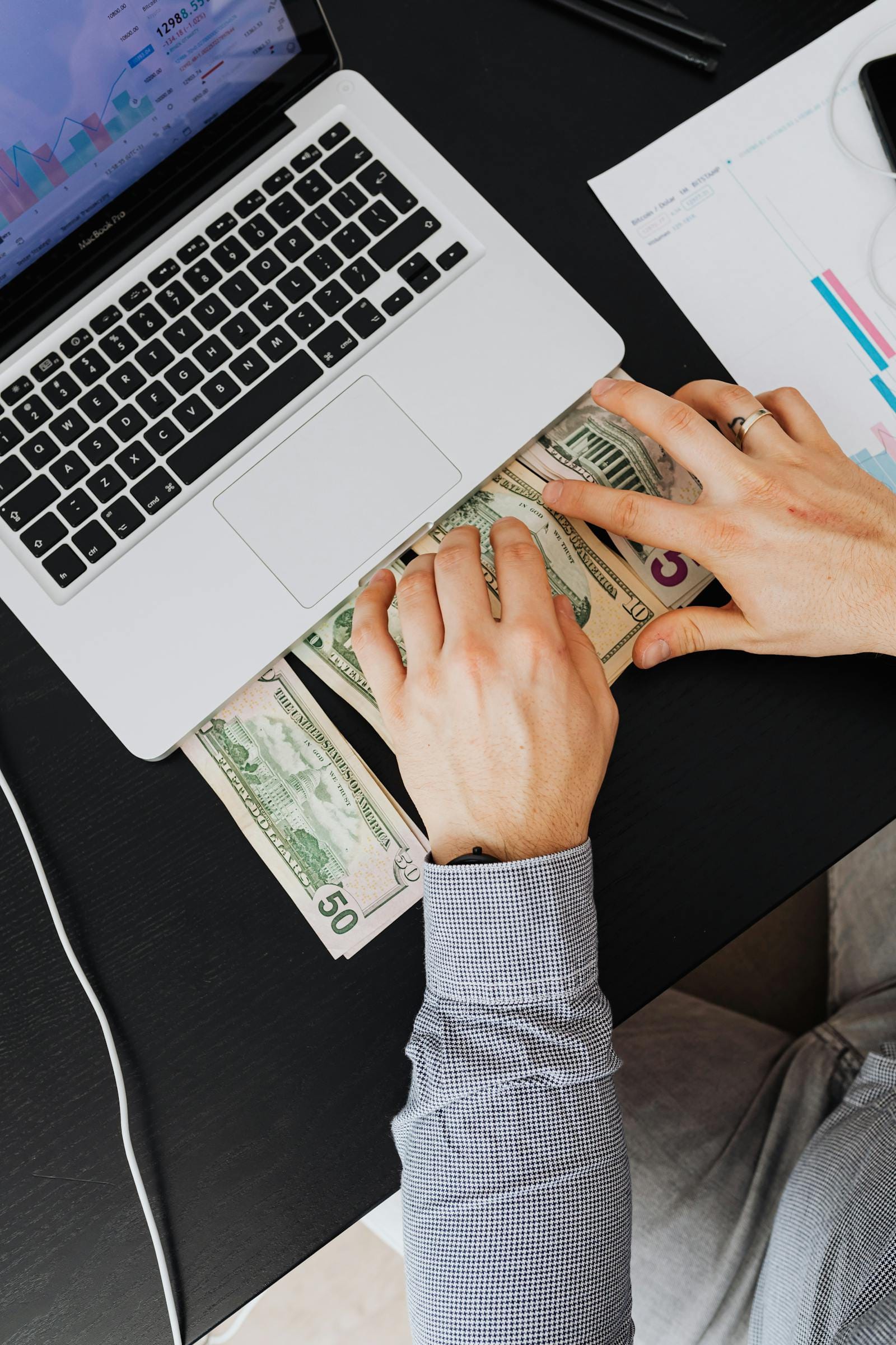 Person counting money next to laptop with charts, illustrating Upwork vs Fiverr earnings