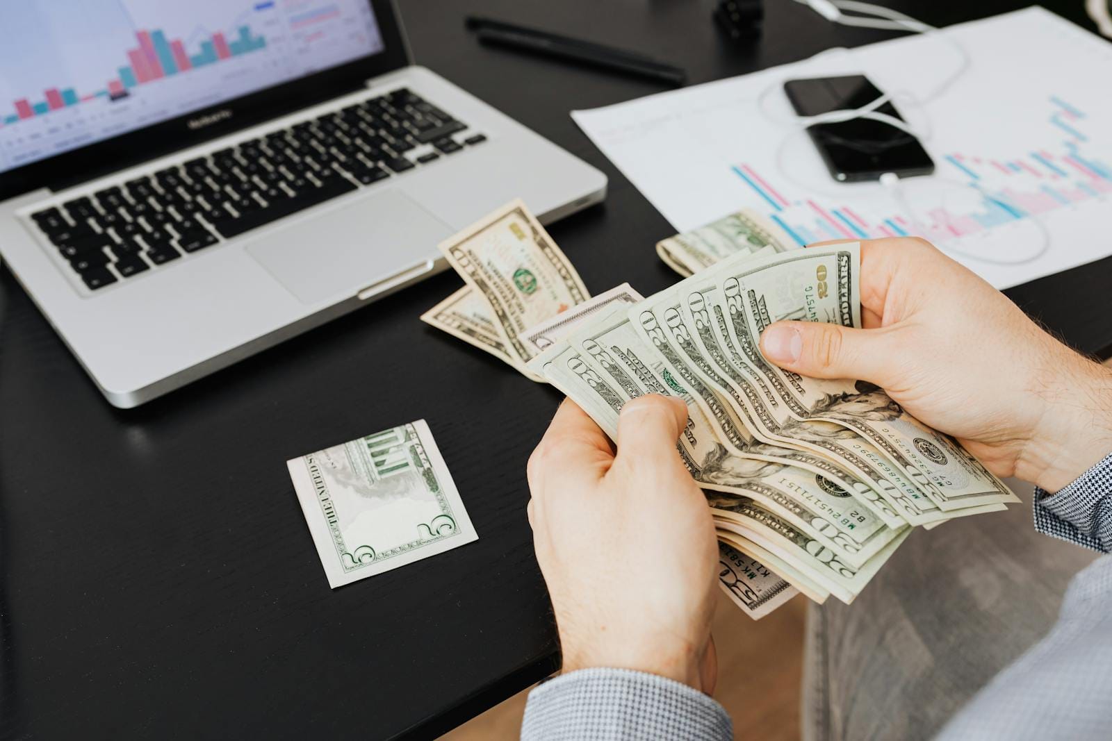Person counting cash beside laptop with charts, illustrating first $1,000 month side income