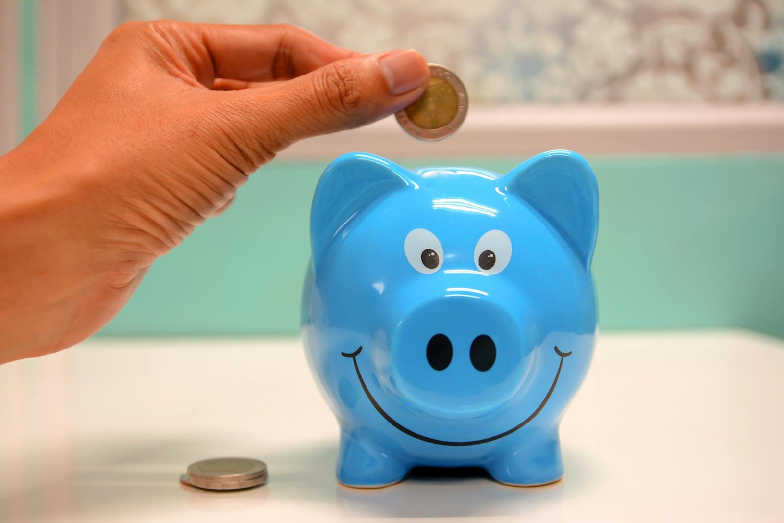 Hand inserting coin into blue piggy bank, illustrating money management and saving