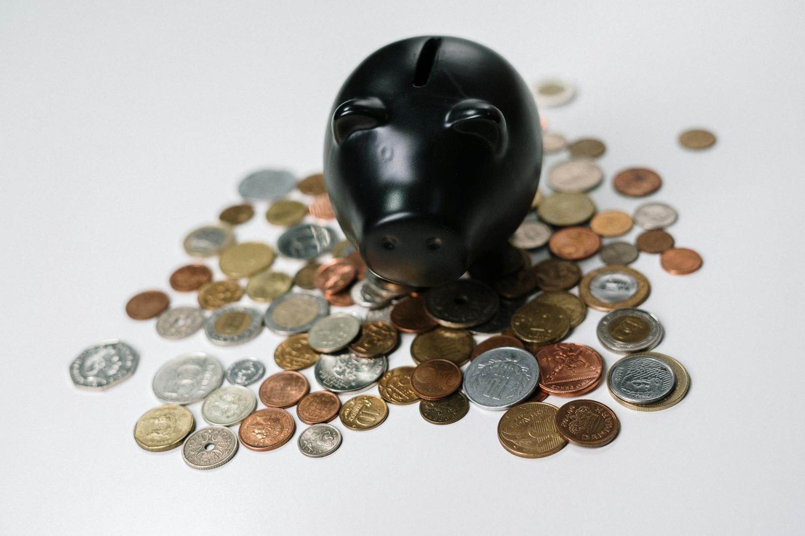 Piggy bank surrounded by various coins on white surface, illustrating Acorns micro-savings concept
