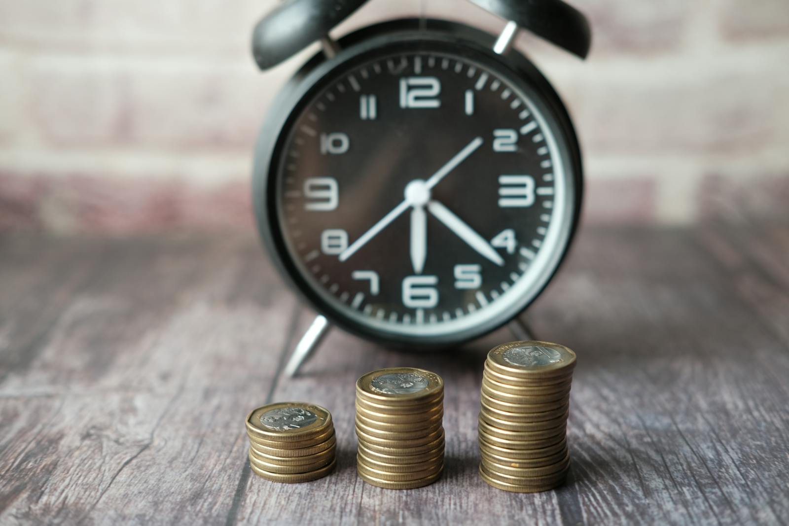 Stacked coins and classic alarm clock on dark surface, illustrating long-term compounding savings via Acorns