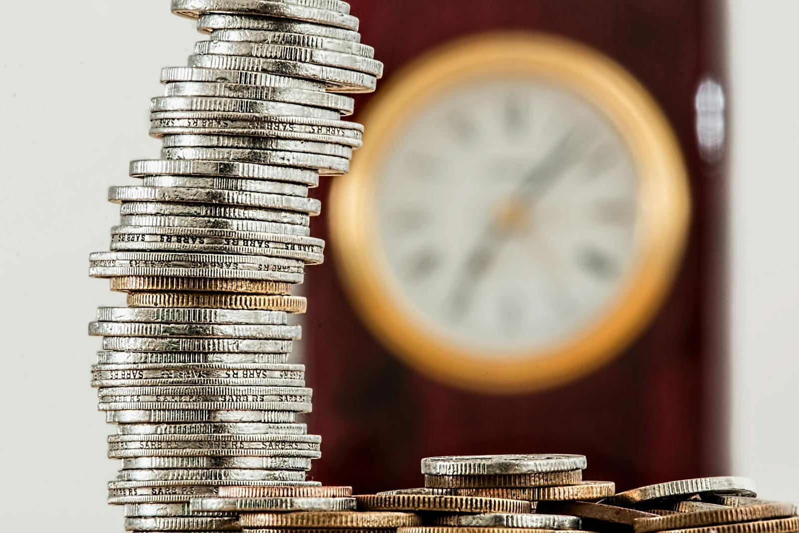 Close-up of stacked coins with blurred clock, illustrating compounding investments over time