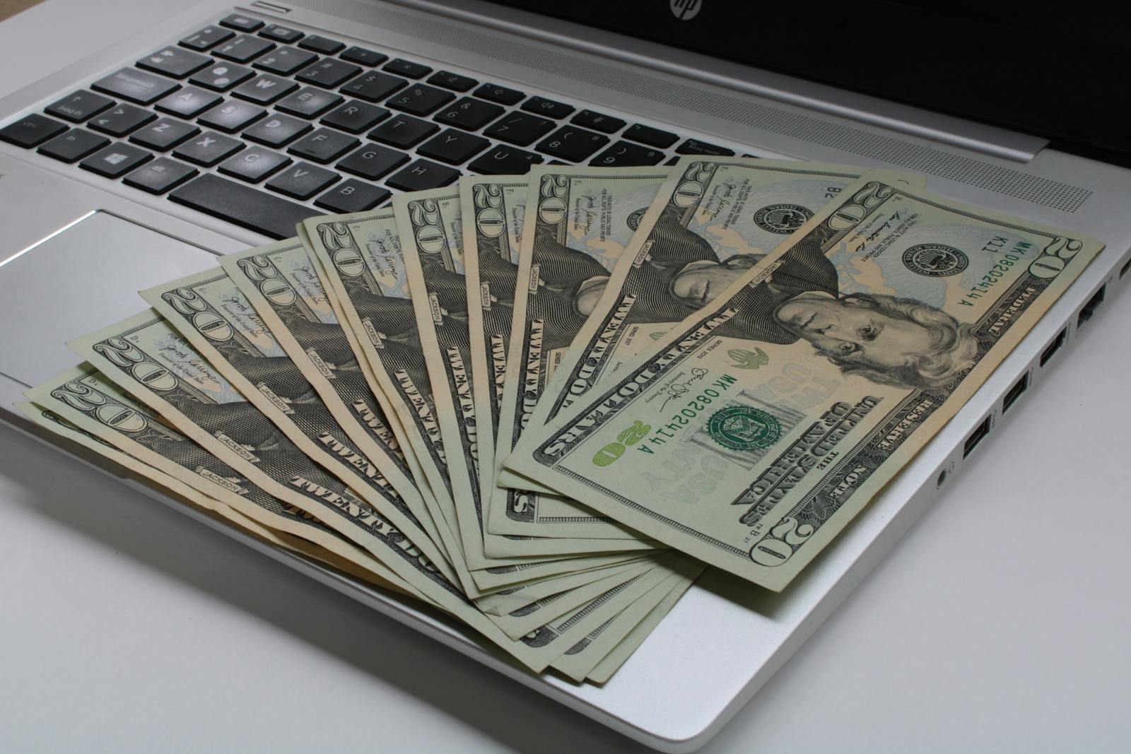 Stack of US dollar bills on laptop keyboard, illustrating credit savings