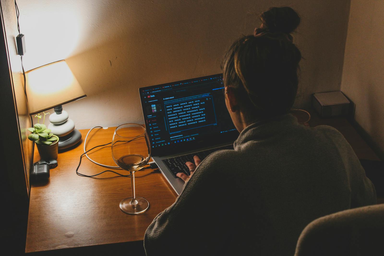Person working from home at night, typing on laptop with soft lamp lighting