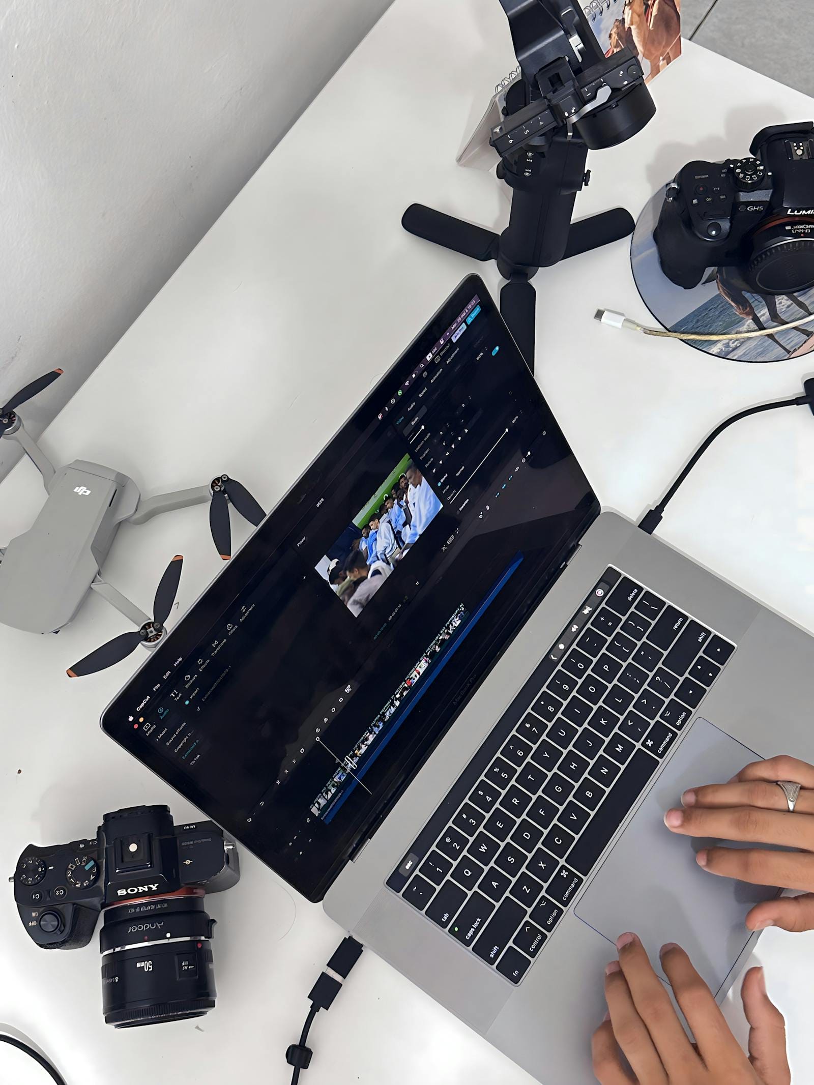 Hands editing aerial footage on laptop with camera, drone, and stabilizer