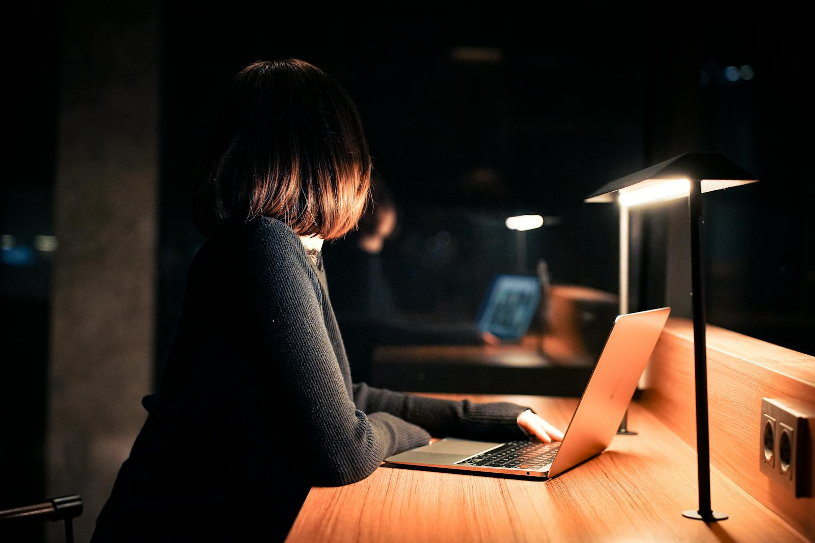 Woman works on laptop under warm lighting, calm nighttime atmosphere