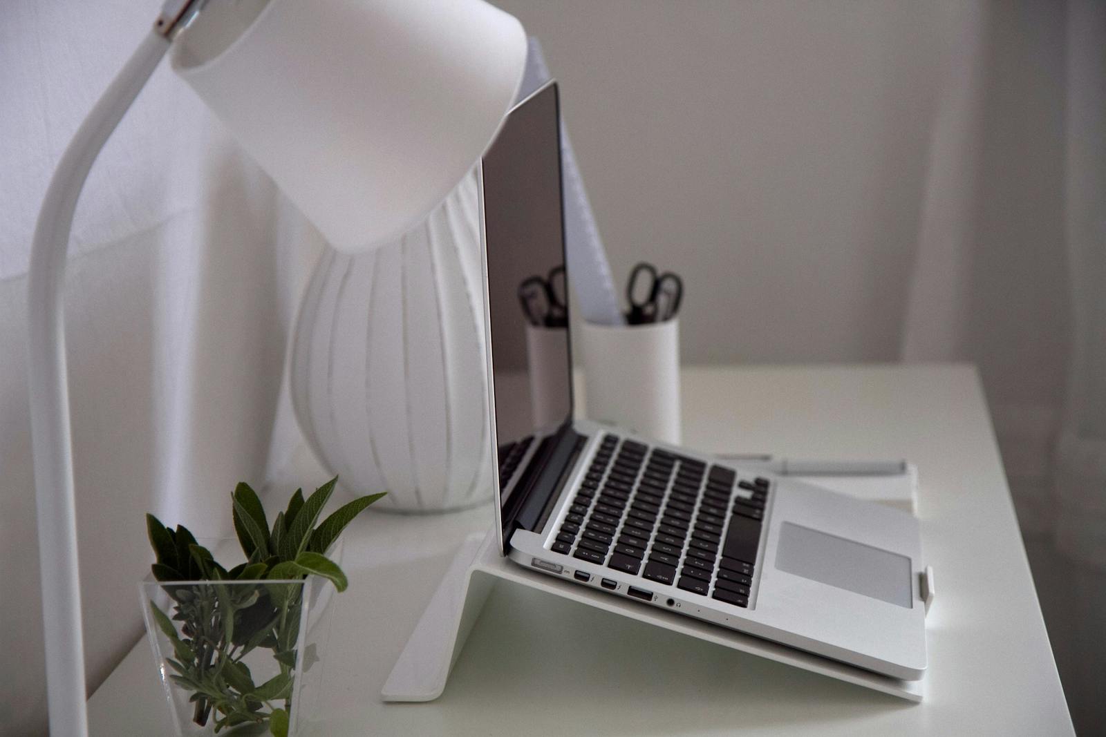Modern home office with laptop, desk lamp, and plant on white desk