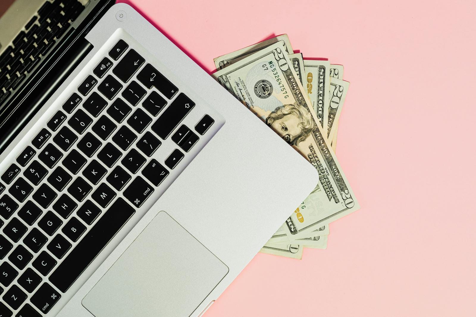 Laptop keyboard with dollar bills on a pink surface, symbolizing online business