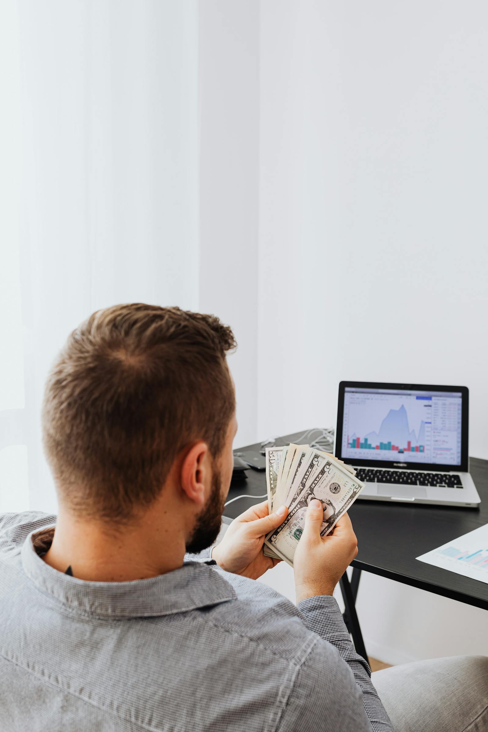 Businessman holding money while analyzing stock market data on laptop