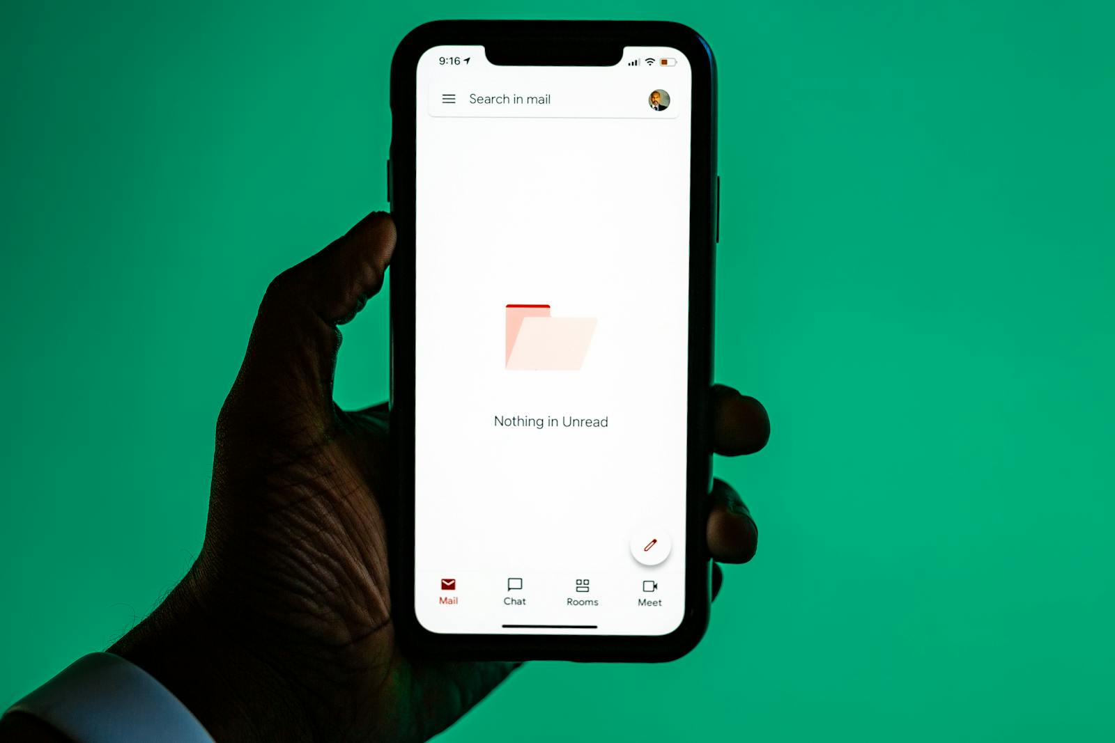 Hand holding smartphone displaying email app against green background