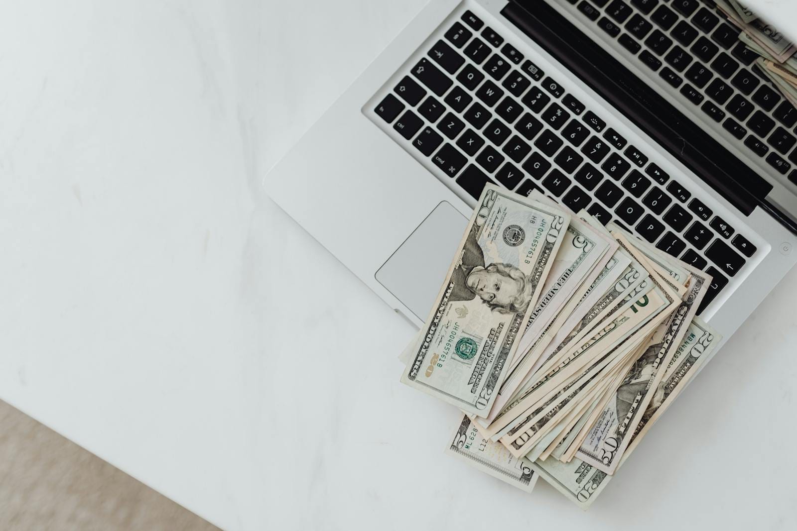 US dollar bills scattered on laptop keyboard on white desk, digital finance